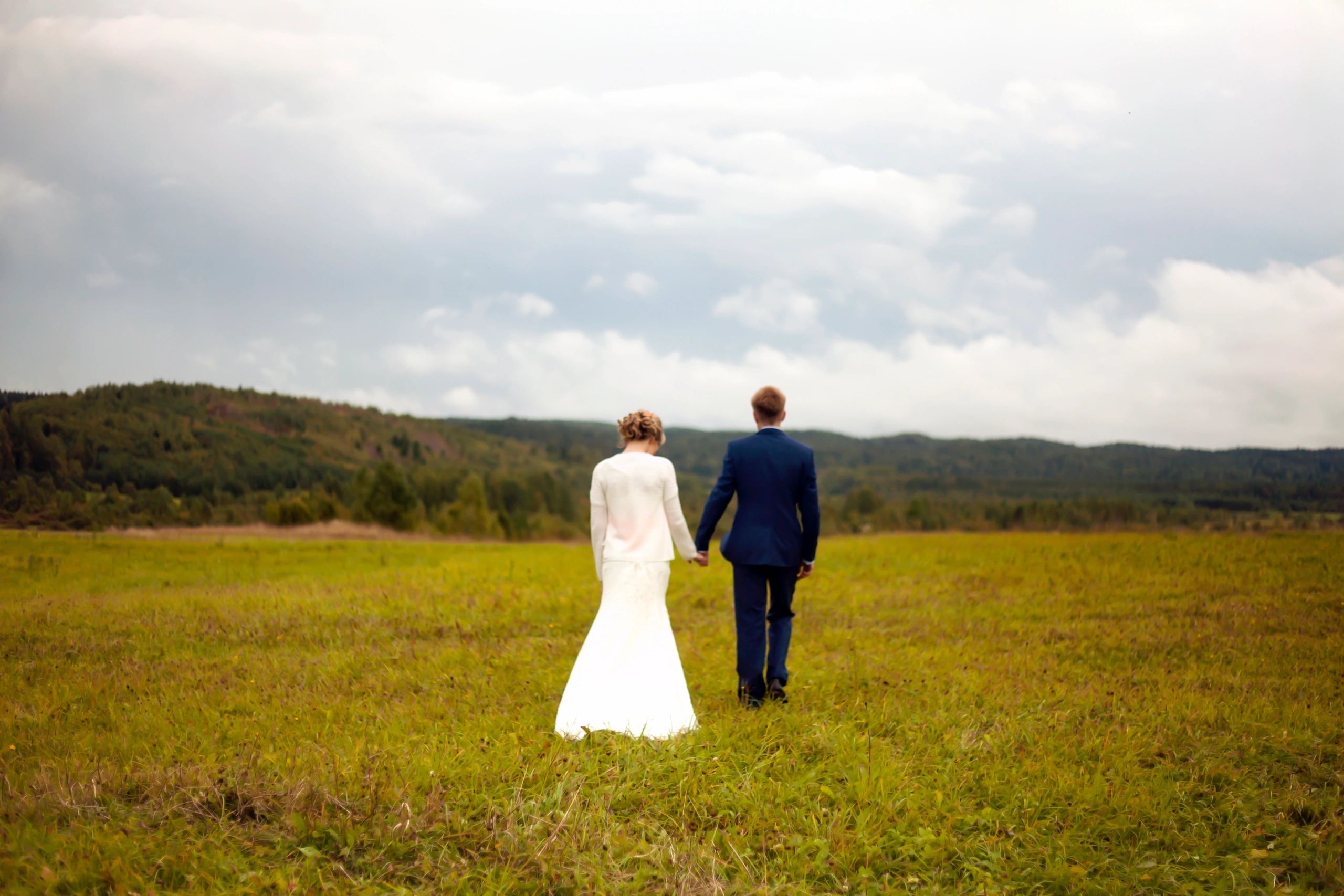 Bride and groom walking hand in hand through an open field